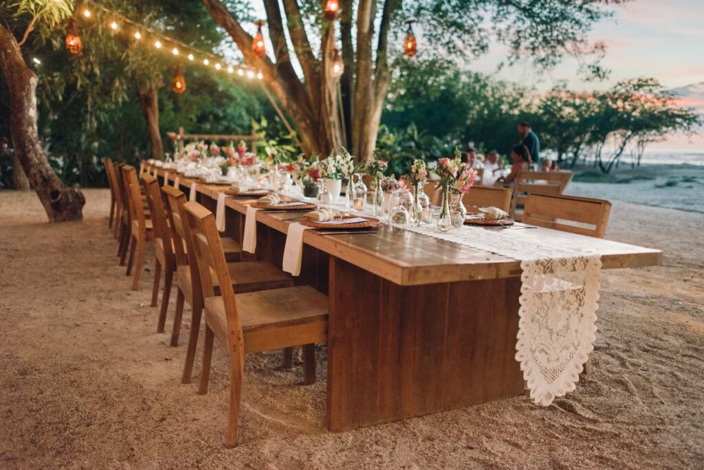 costa rica A beautiful photo of a long wooden table set up on the beach at sunset, perfect for a romantic wedding.