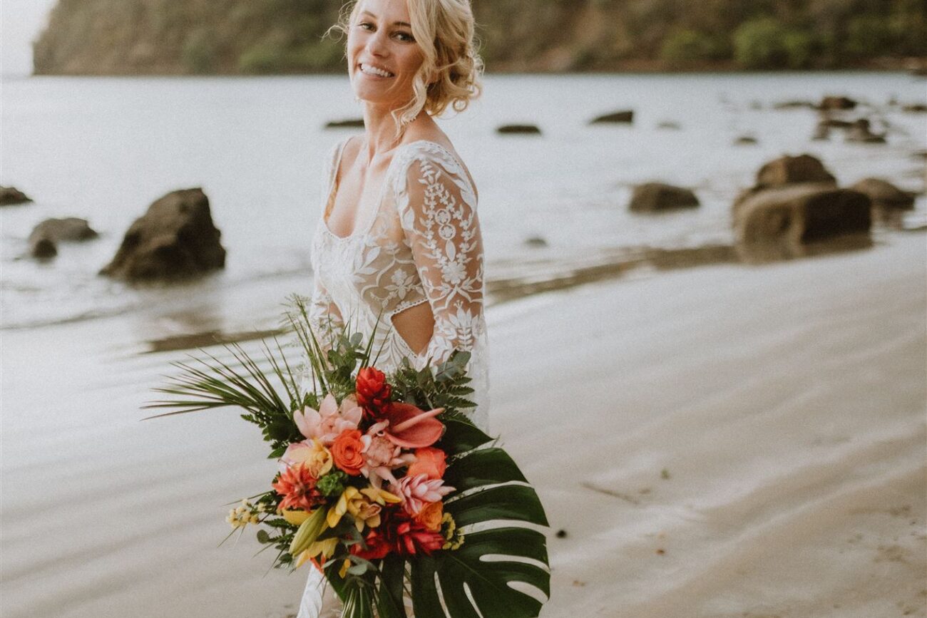 costa rica A woman in a white dress holding a bouquet of flowers on a beach in Costa Rica.