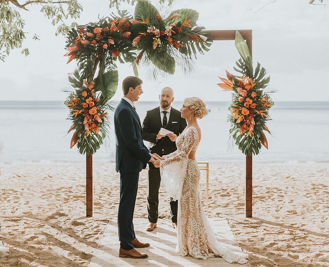 costa rica A newlywed couple holding hands under a beach arch, captured in a beautiful wedding photo by a talented Costa Rica photographer.