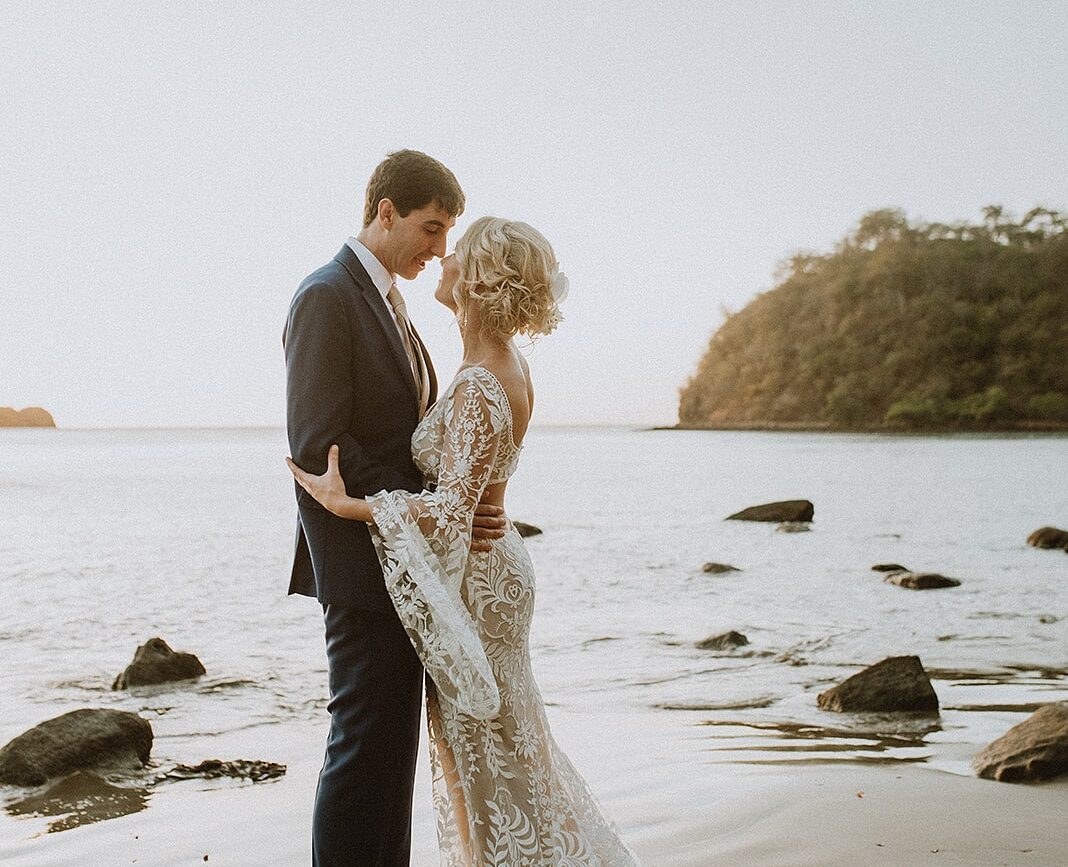 costa rica A wedding photo of a bride and groom standing on rocks at sunset at Playa.