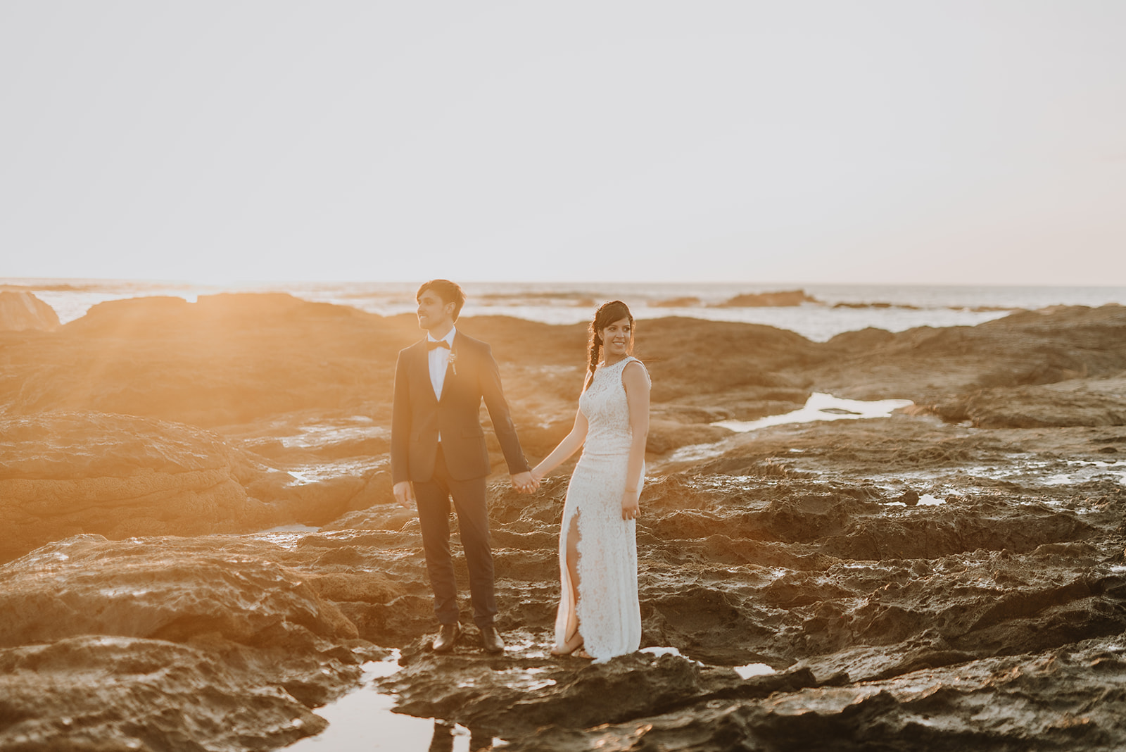 costa rica A stunning wedding photo of a bride and groom standing on rocks at sunset, captured by a talented Costa Rica photographer.