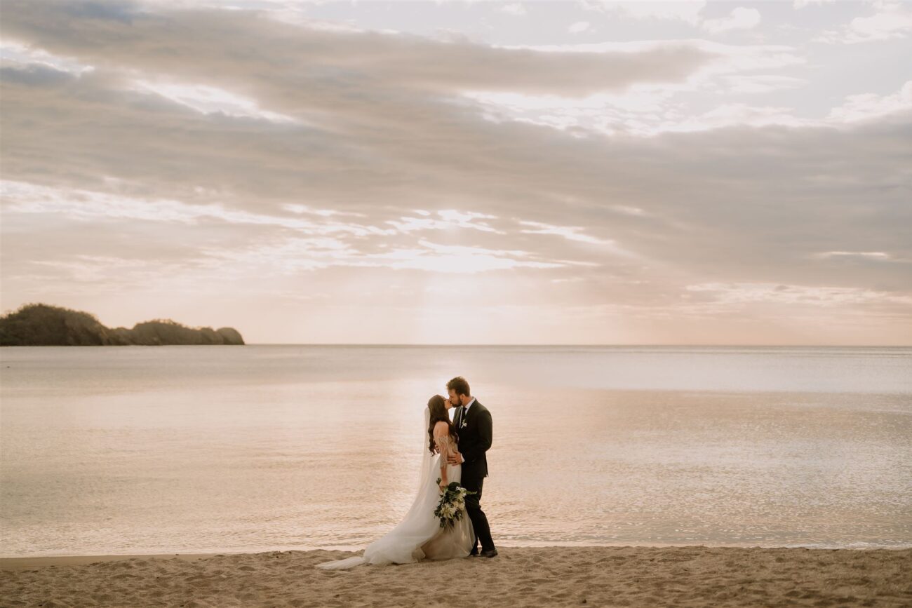 costa rica A wedding photo of a bride and groom standing on the playa at sunset.