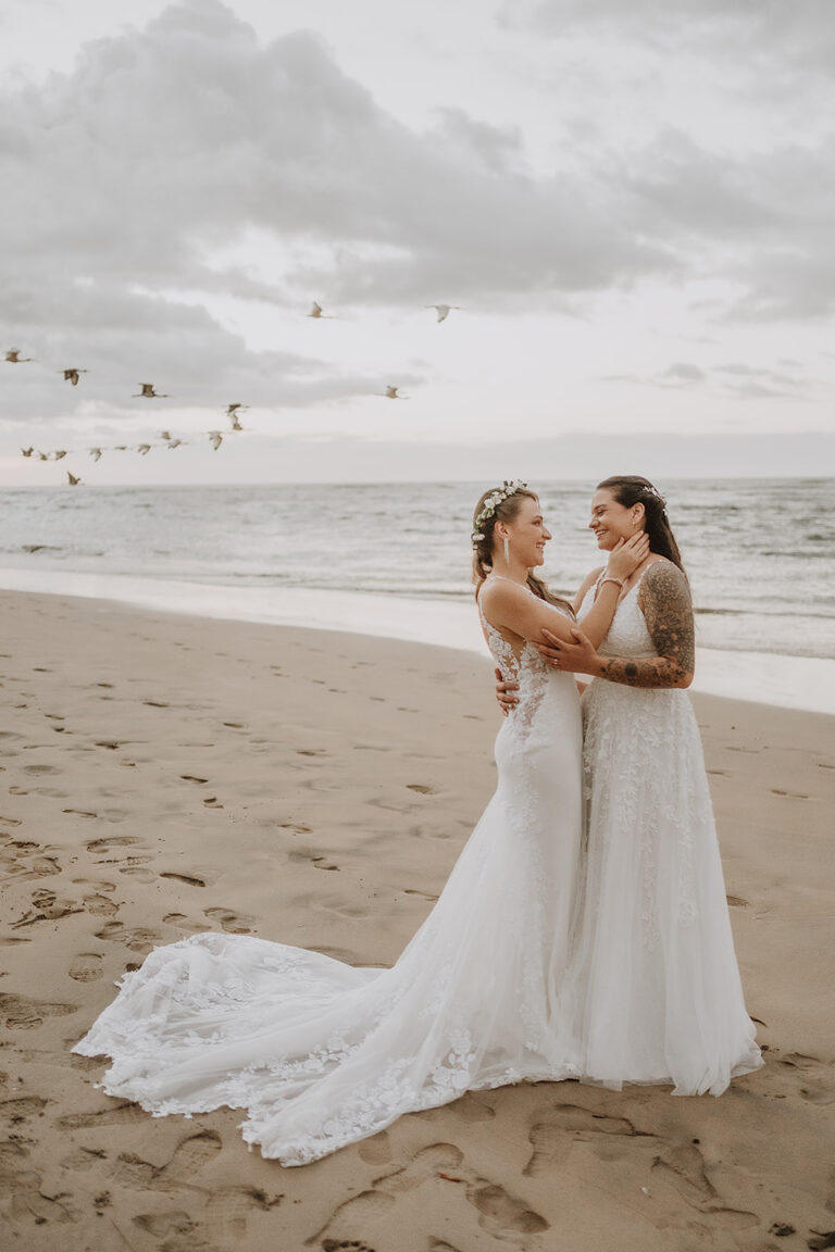 costa rica Two brides standing on the playa with birds flying around them, captured beautifully by a Costa Rica wedding photographer.