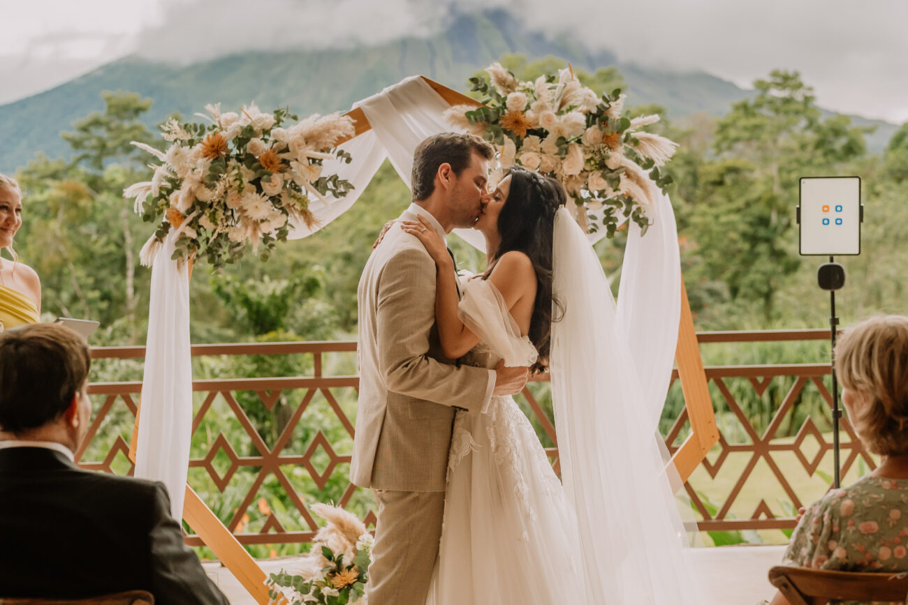 costa rica A bride and groom kiss in front of a mountain during their wedding ceremony captured by a Costa Rica photographer.