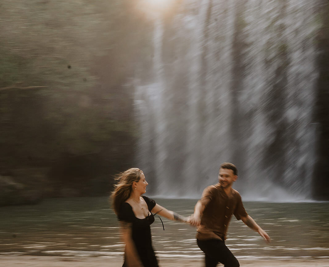 costa rica A man and woman capturing their engagement photos while running in front of a picturesque waterfall in Costa Rica, amid the breathtaking scenery of the top waterfall.