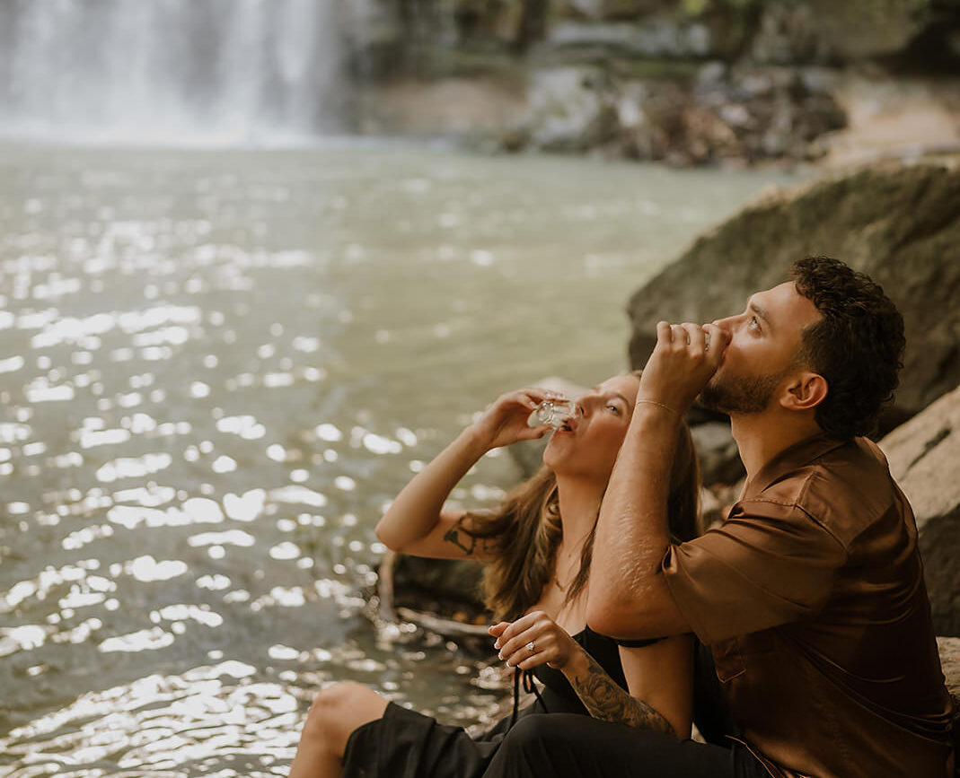 costa rica A man and woman sitting on a rock near a waterfall in Costa Rica for their engagement photos.