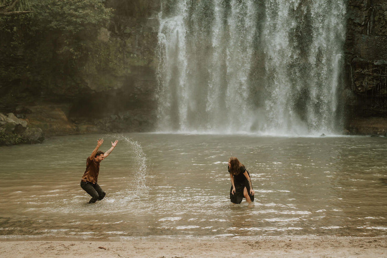 costa rica A couple poses for their engagement photos, joyfully playing in the crystal-clear waters of a stunning Costa Rican waterfall.