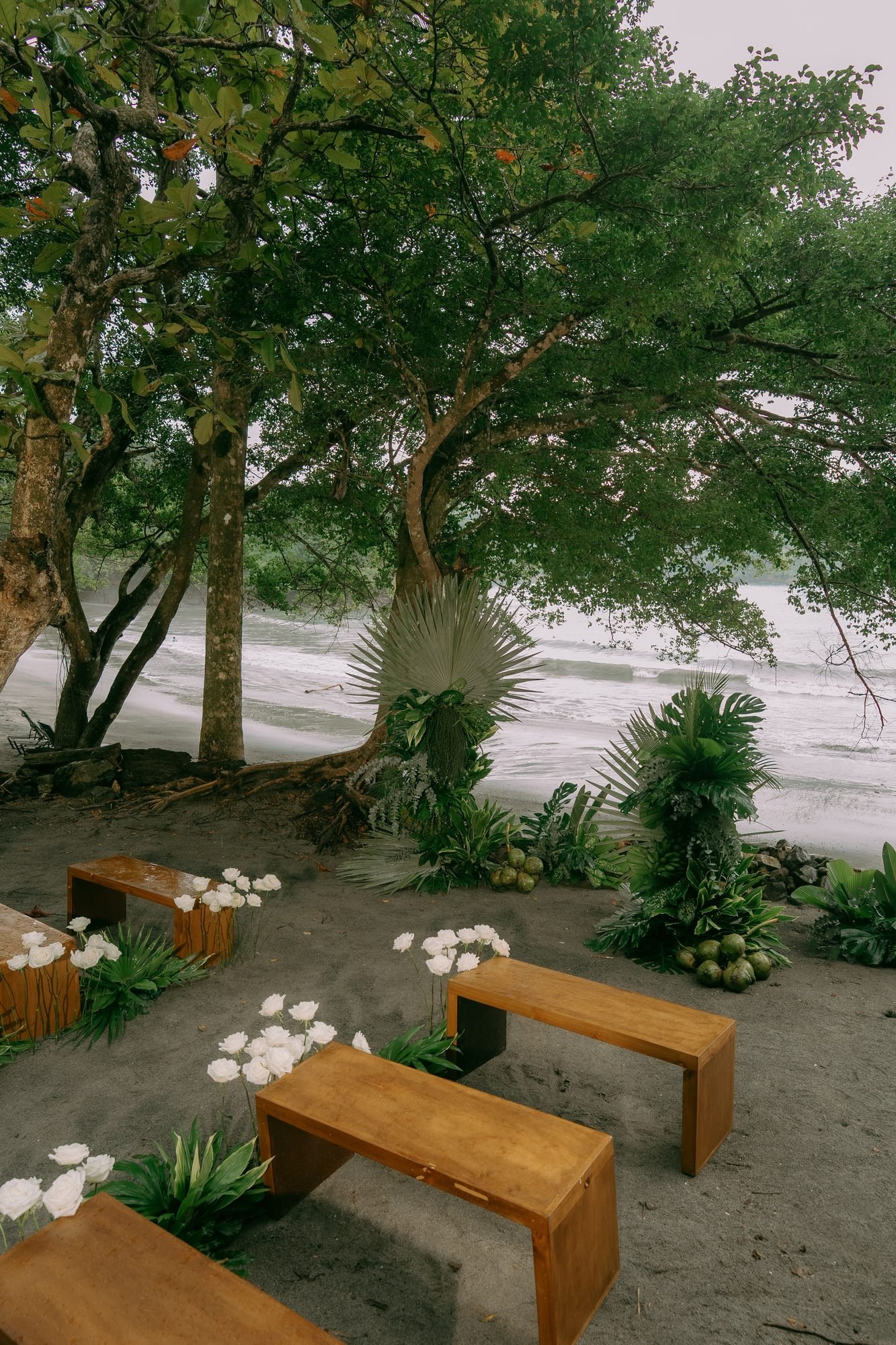 Wooden benches and white floral arrangements set up for a small ceremony beside the water