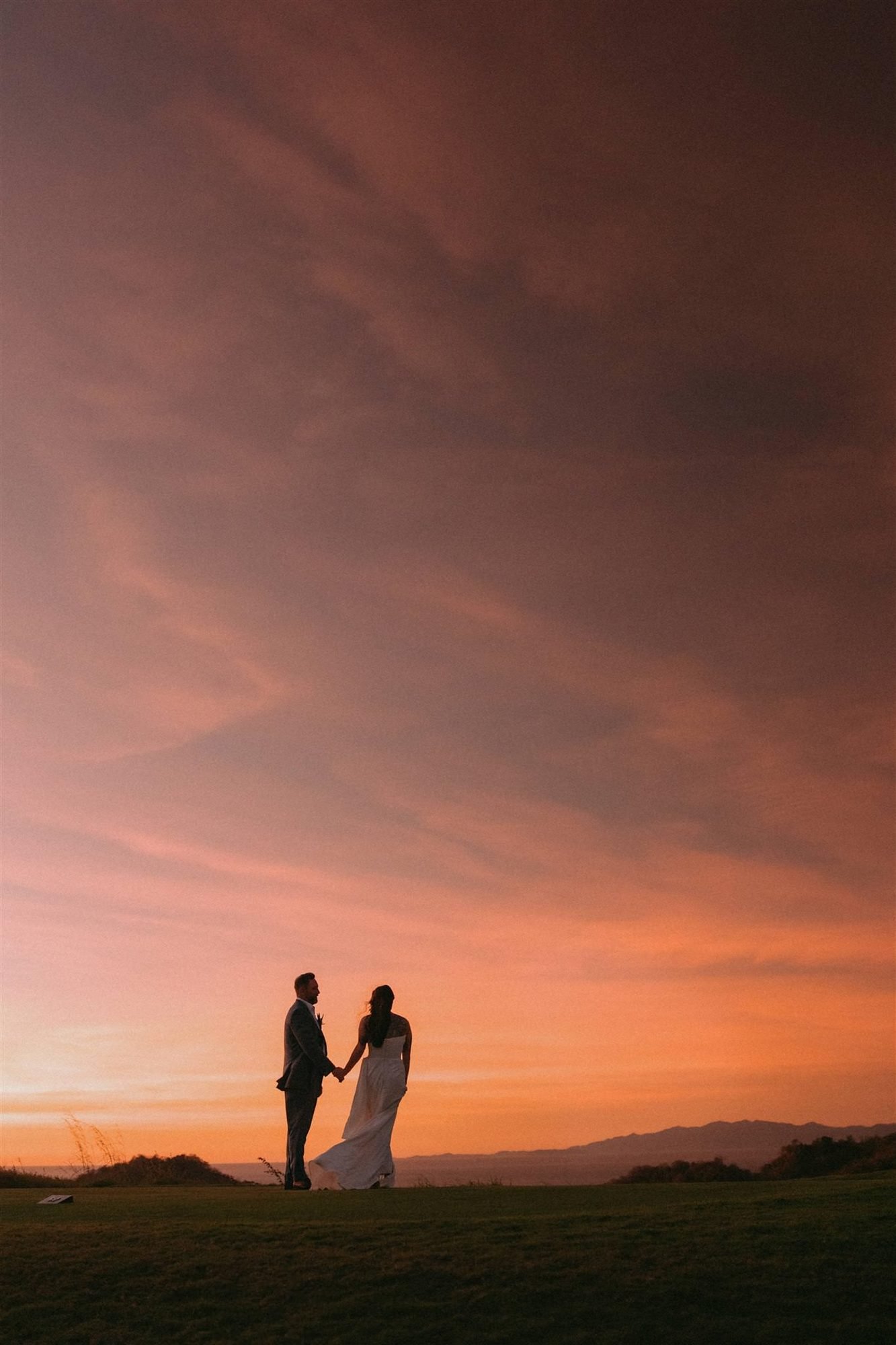 A couple stands in silhouette against a vivid orange and pink sunset sky in Costa Rica