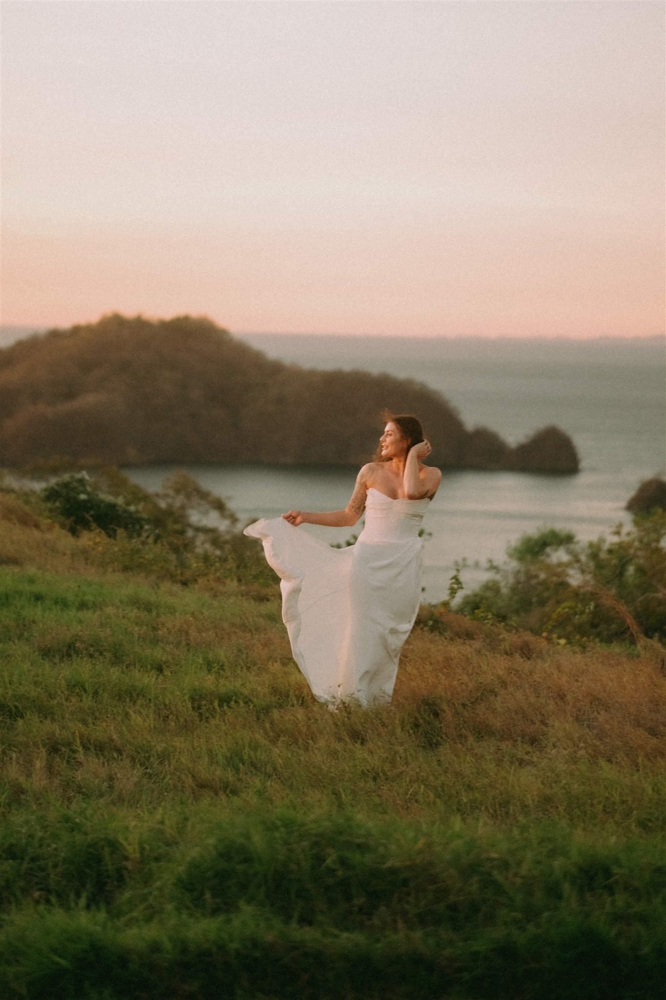 A bride stands on a green headland above the Pacific coastline in Guanacaste at golden hour