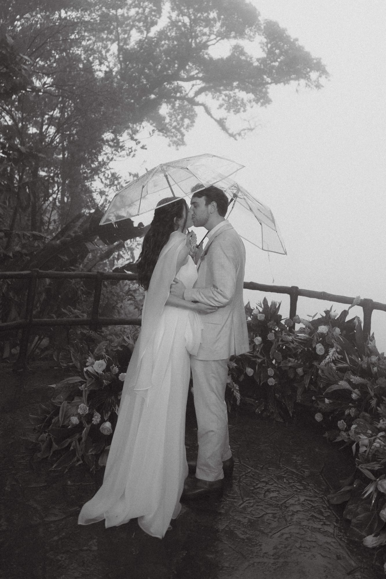 A couple kisses beneath a clear umbrella in the rain, in black and white, photographed by a Costa Rica elopement photographer