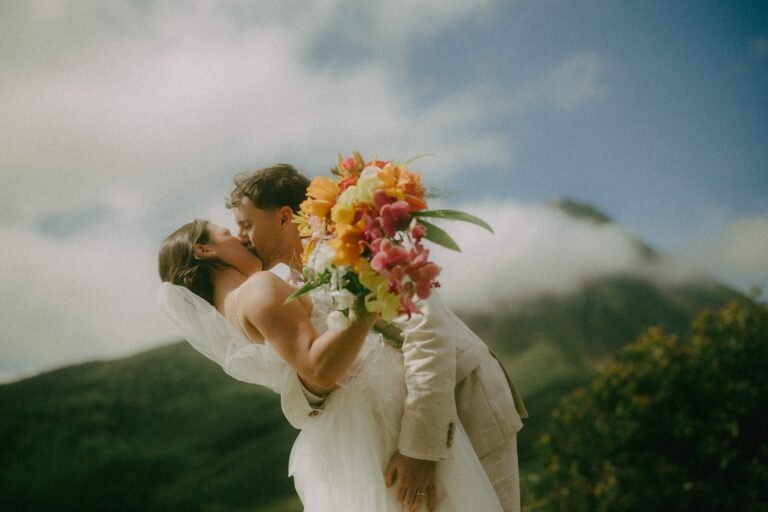 Costa Rica Elopement Photographer 1 A couple kisses as the bride lifts a bright tropical bouquet, green volcano slopes behind them