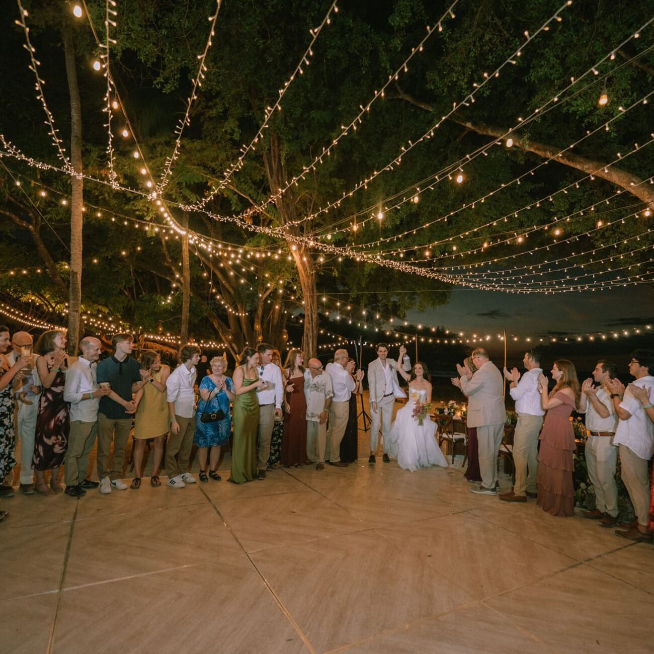 Guests forming a circle around the dance floor under string lights at a Pangas Beach Club wedding