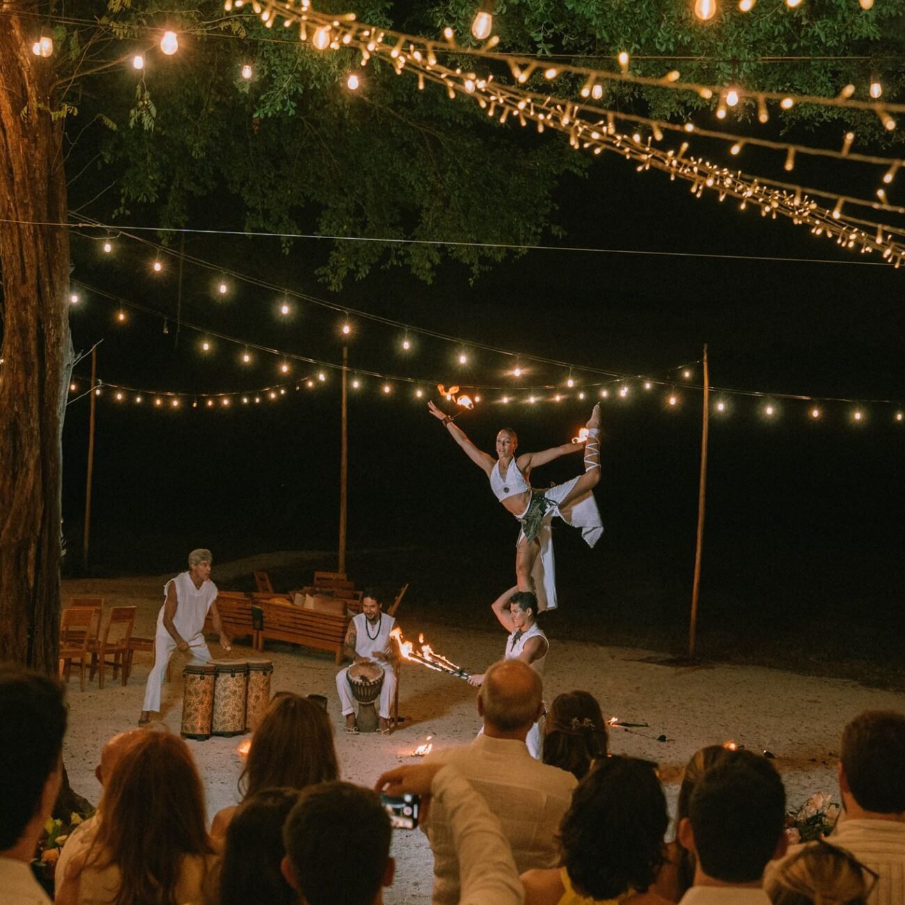 Fire dancers performing on the sand under string lights while guests watch at Pangas Beach Club