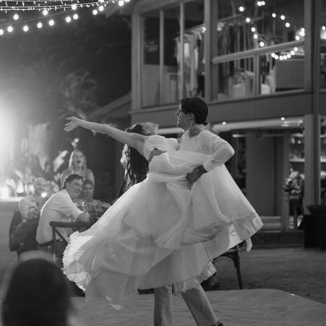 The couple dancing under string lights at the reception