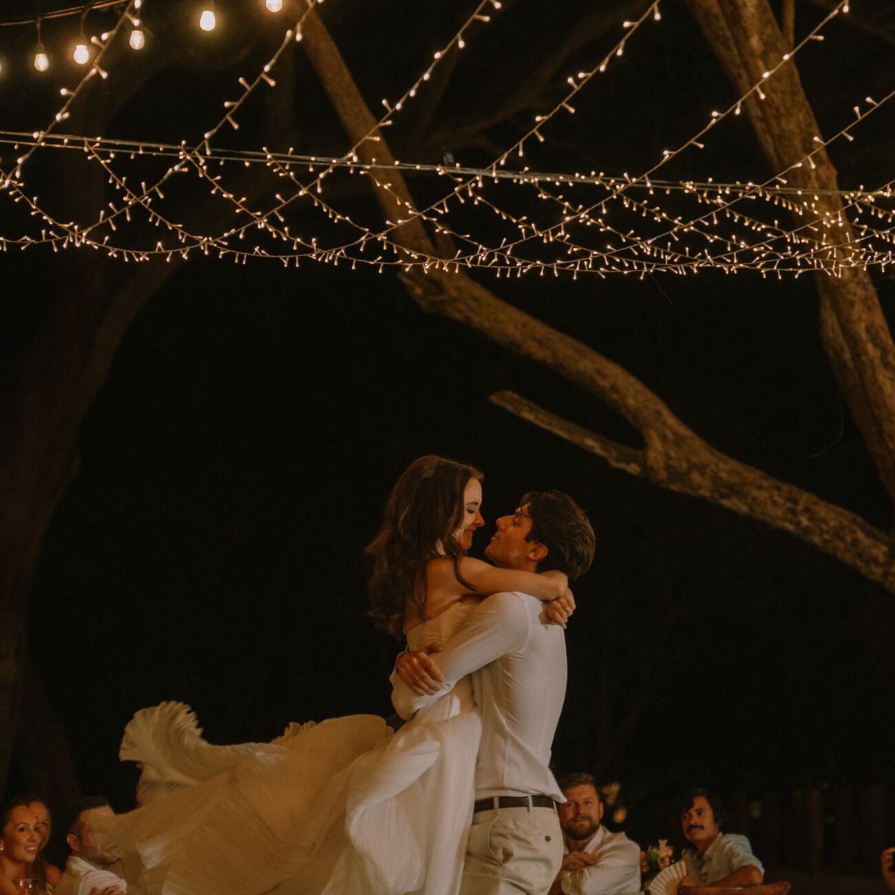 The groom lifting the bride in a dance under string lights