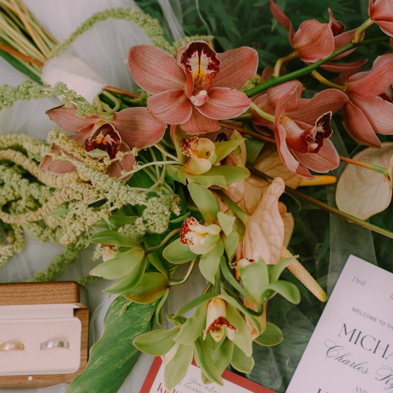 Wedding rings in a box, an invitation and orchid flowers laid on tulle before a Pangas Beach Club wedding