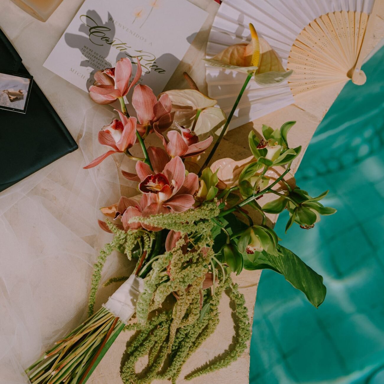 Bouquet, folding fan and printed cards laid flat beside a turquoise pool