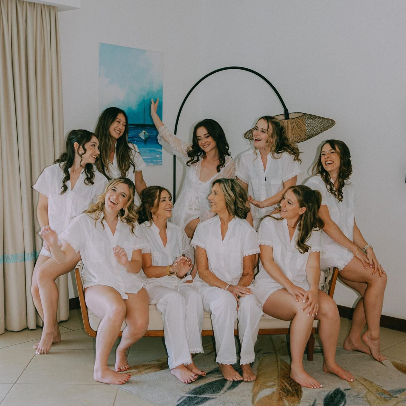 The bride and her best friends in matching white pajamas seated together on a sofa while getting ready