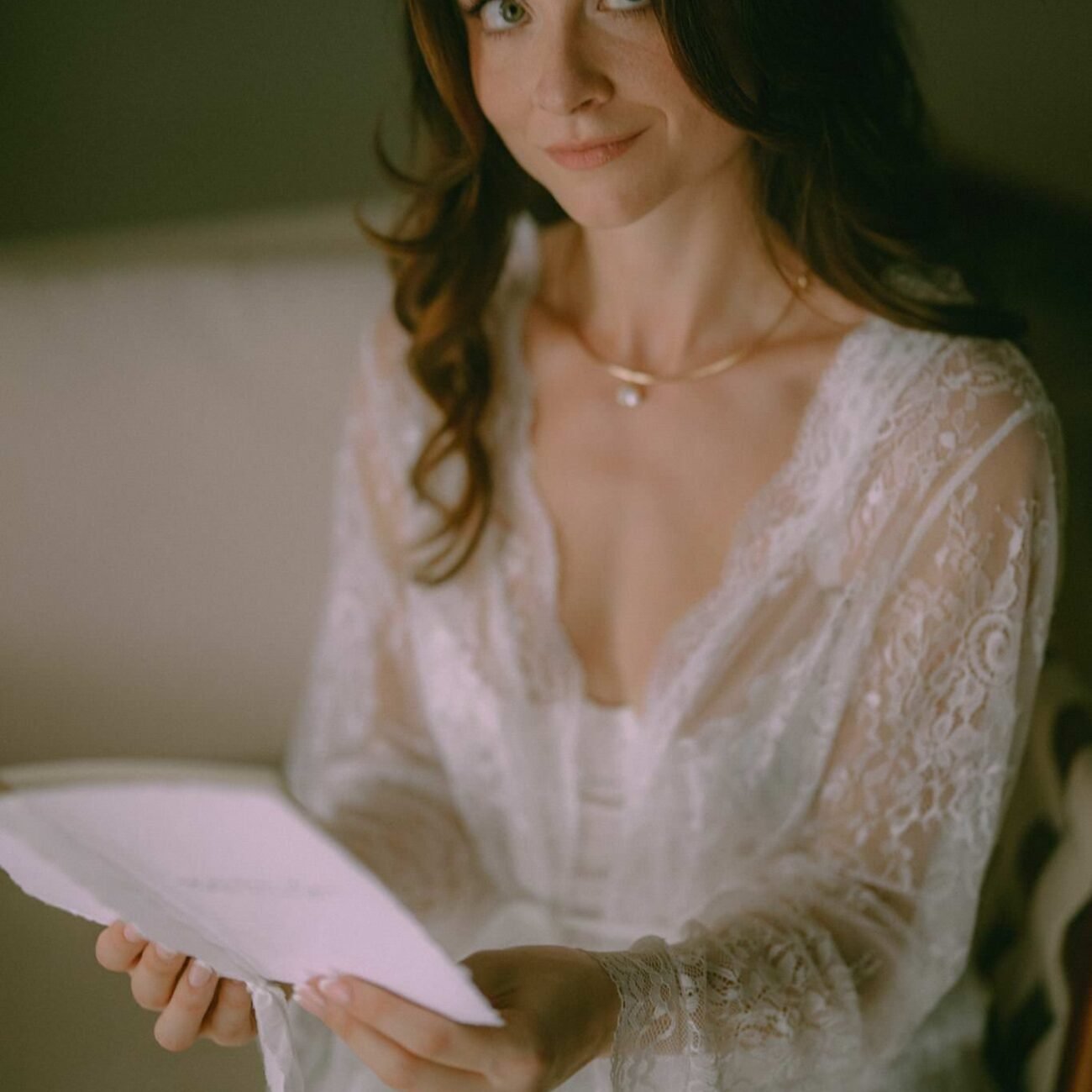 The bride in a lace robe holding a folded letter while getting ready