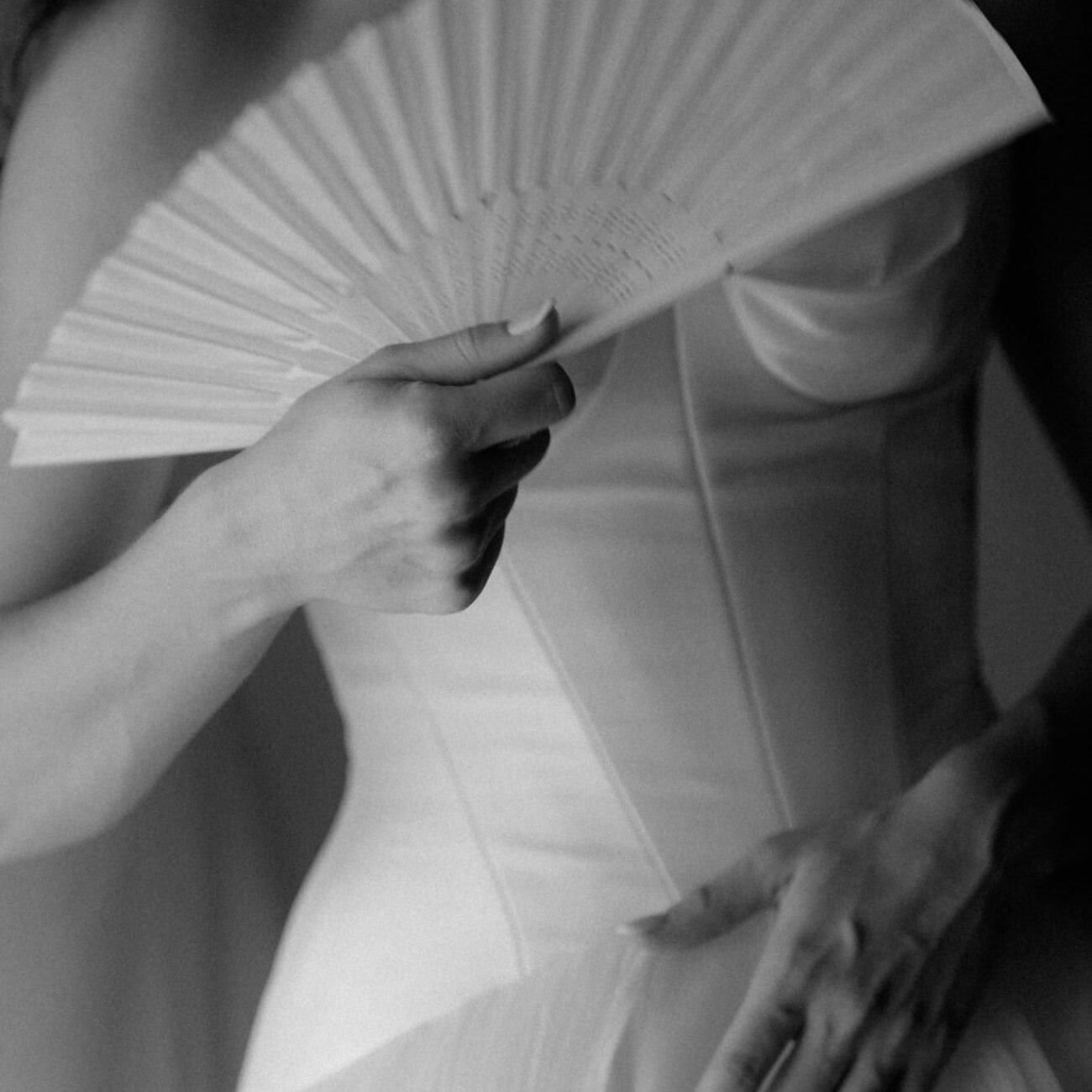 Black and white detail of the bride holding a folding fan against her dress