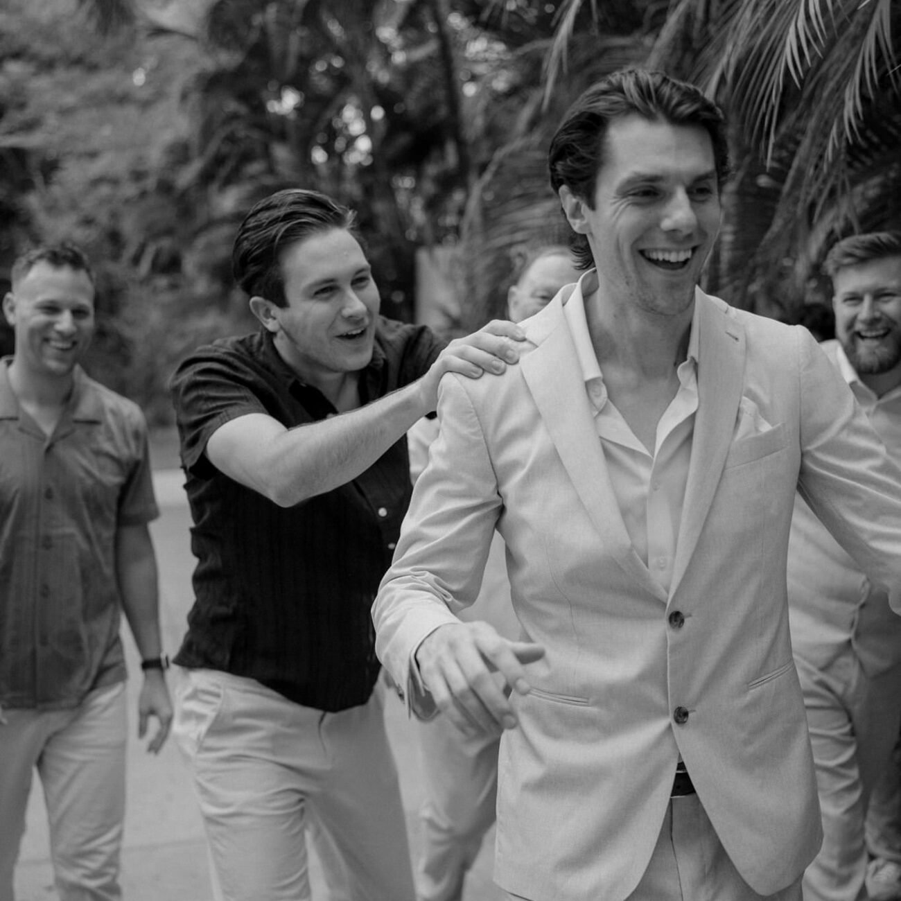 The groom laughing as he walks with friends, black and white