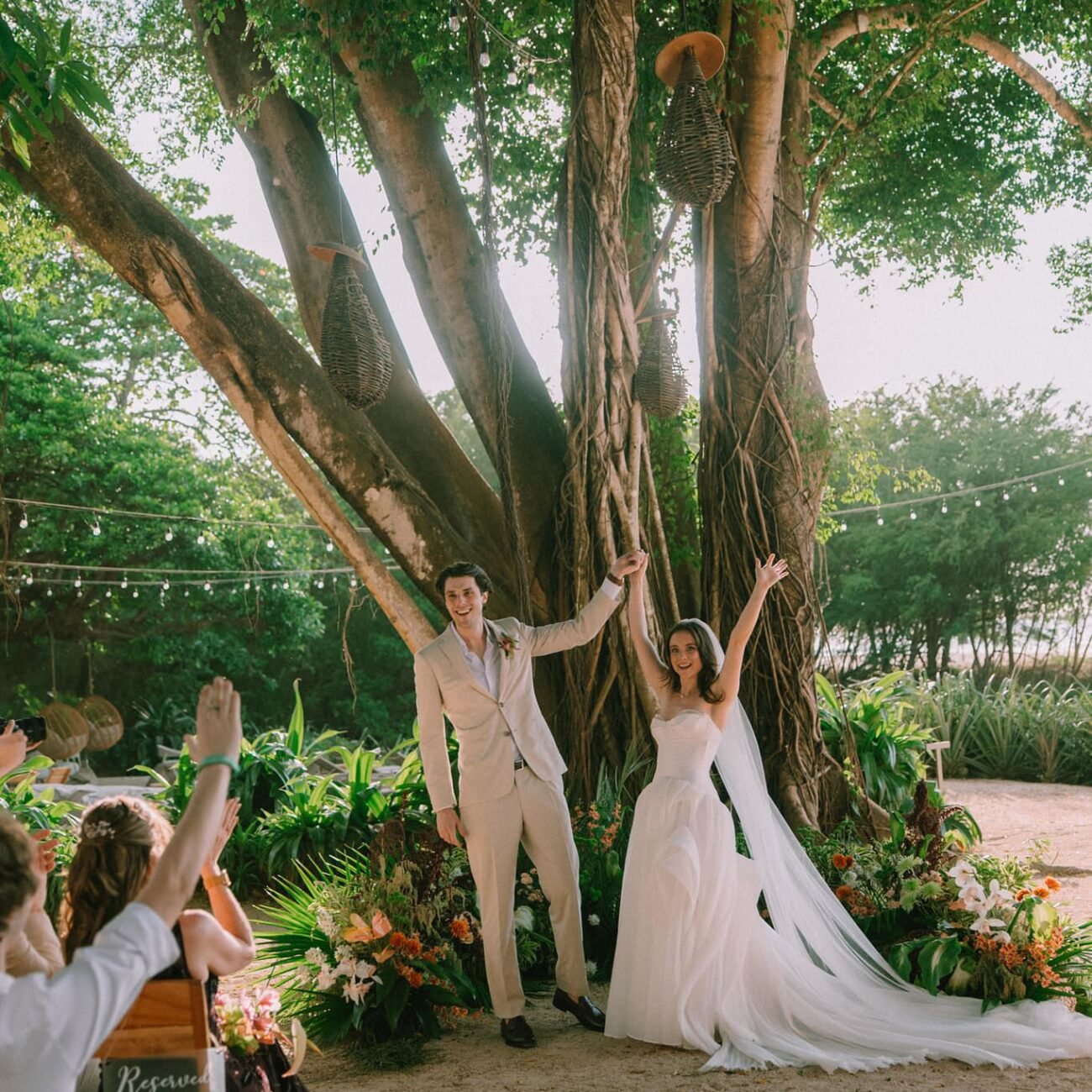 The couple under a large tree with guests cheering around them at Pangas Beach Club