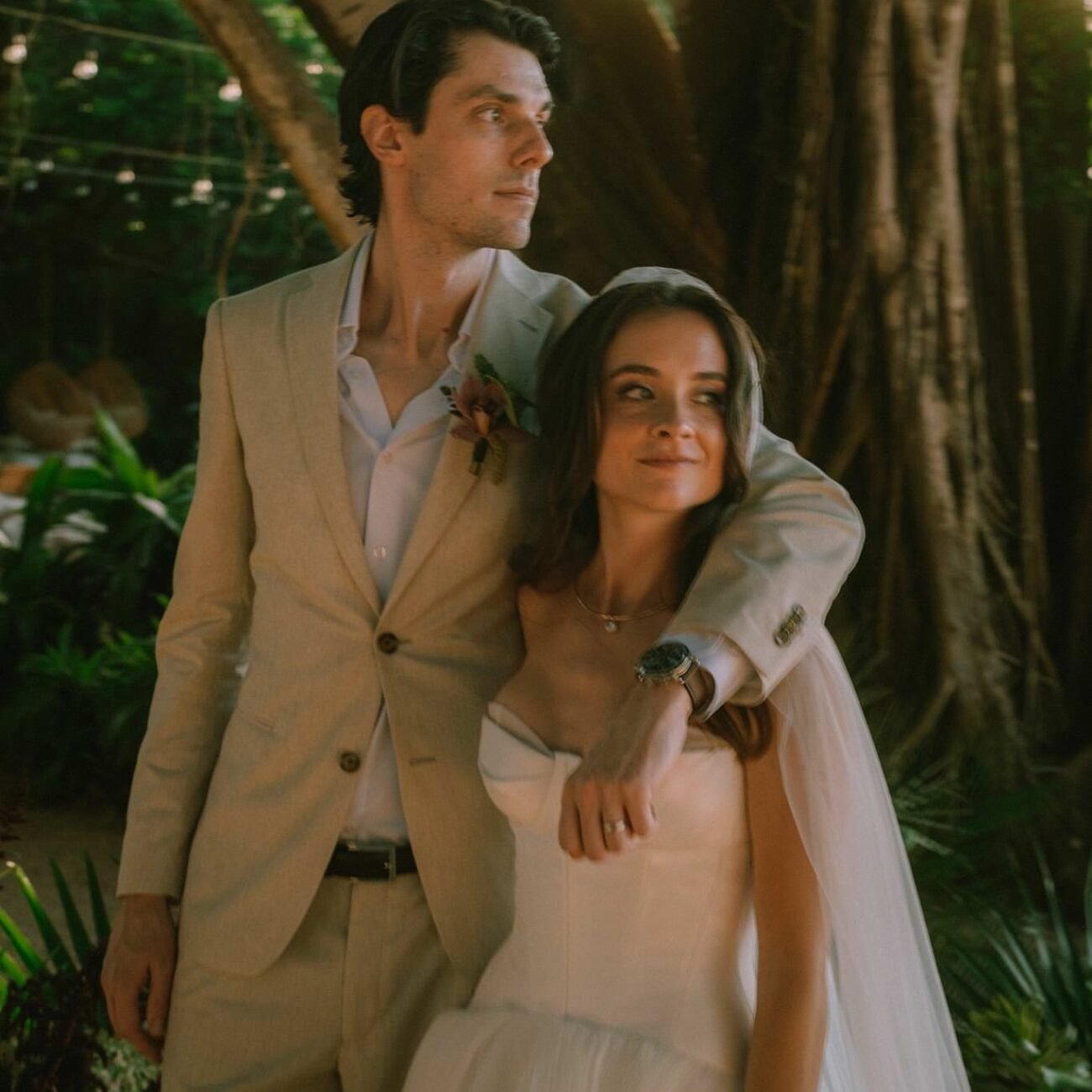 The groom with his arm around the bride under the tree in warm light