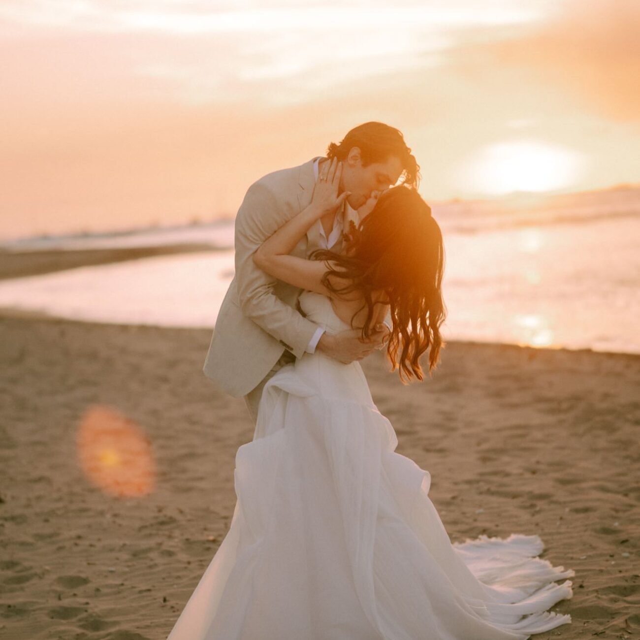 The couple dancing on the sand at sunset, the bride’s dress in motion
