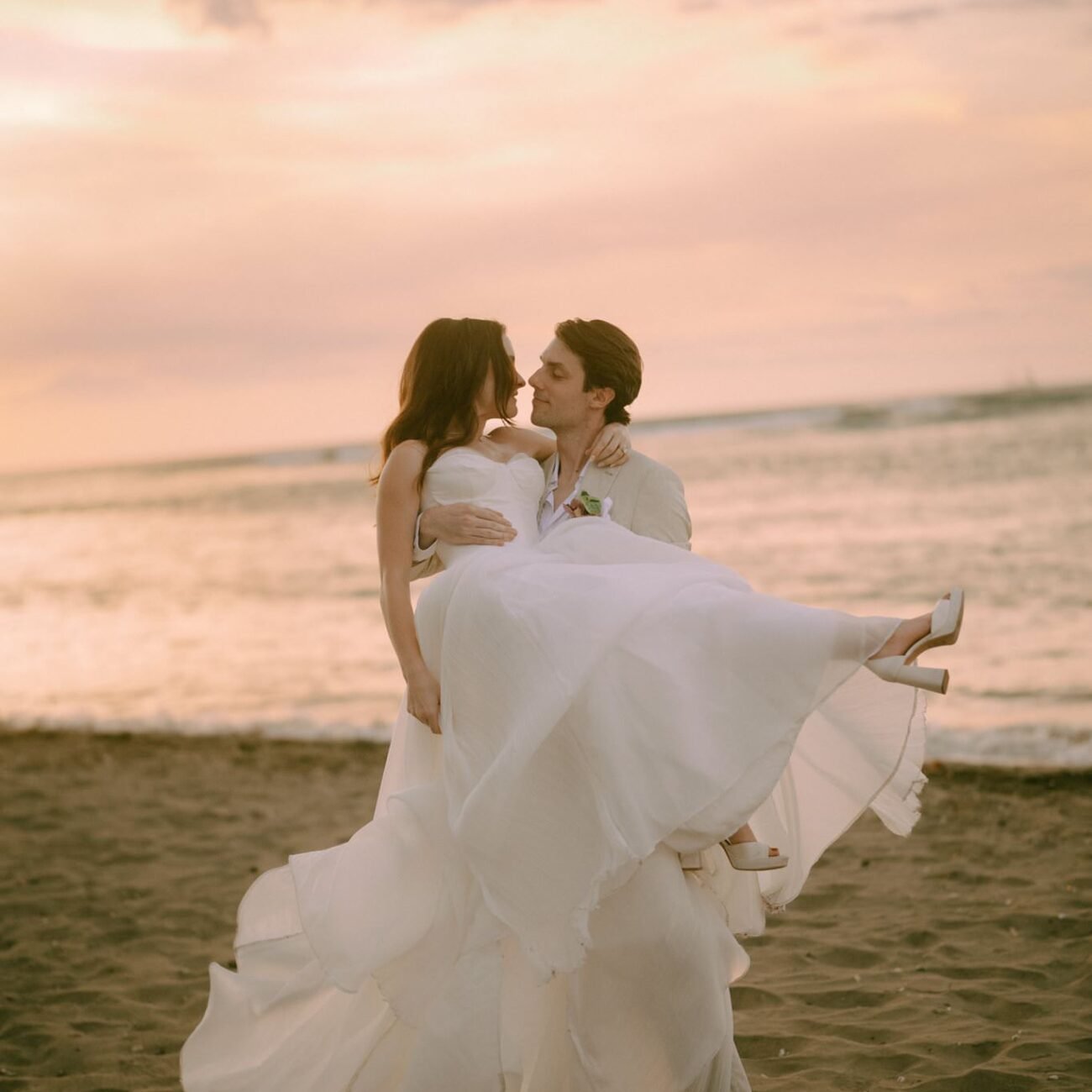The groom lifting the bride on the beach at sunset